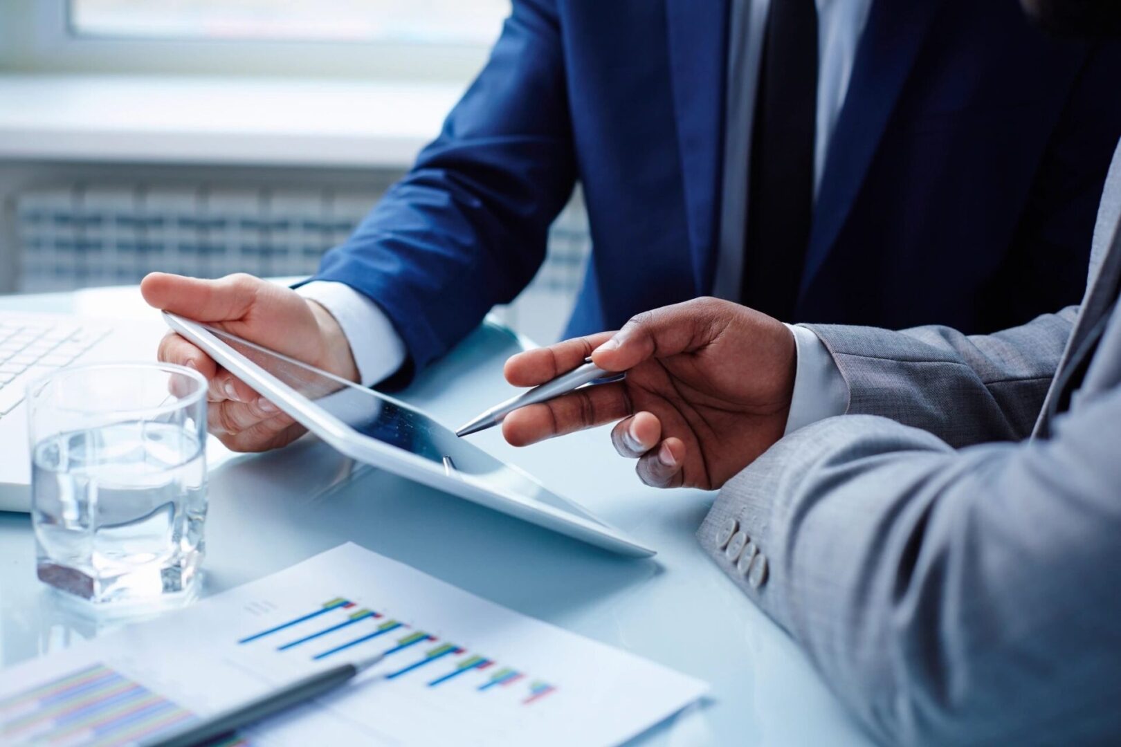 Two people sitting at a table with papers and a tablet.